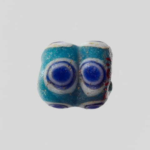 A small turquoise glass bead with two blue eyes ringed in white.