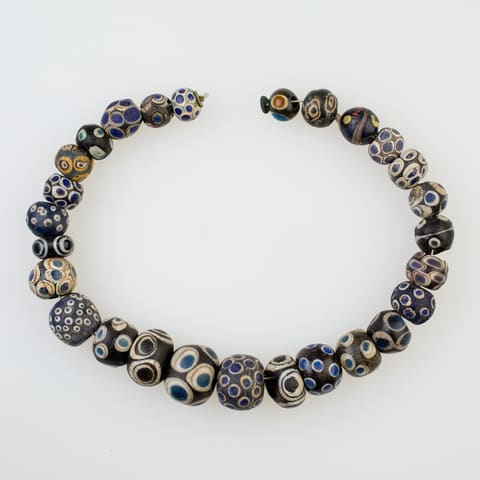A string of 27 glass eye beads laid in an open loop: dark blue and black
beads spotted with white, blue and yellow eyes.